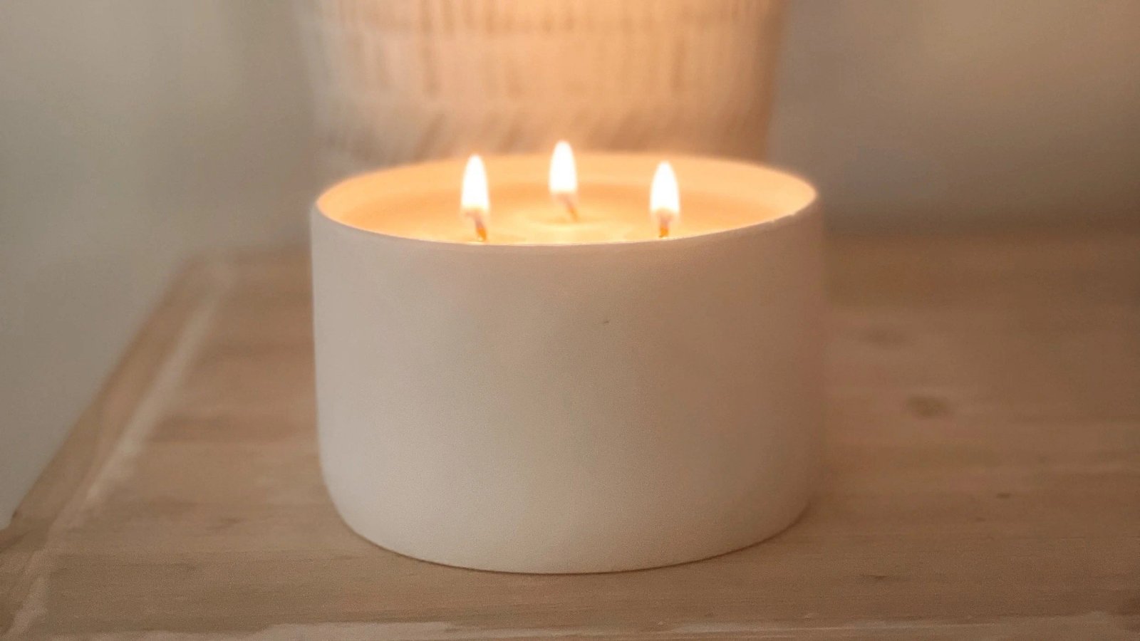 Three-wick candle burning in a round white container on a wooden surface.